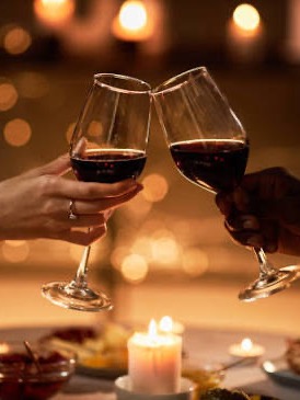 Two people clinking glasses of red wine over a candlelit dinner